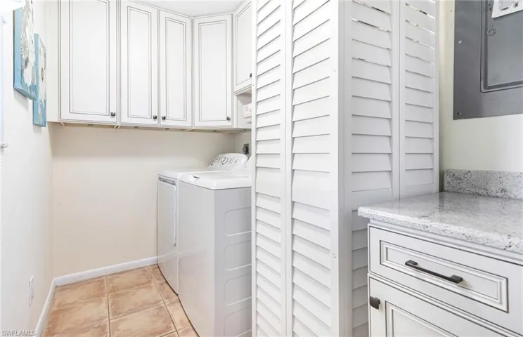 Washroom featuring cabinets, washing machine and dryer, electric panel, and light tile patterned floors