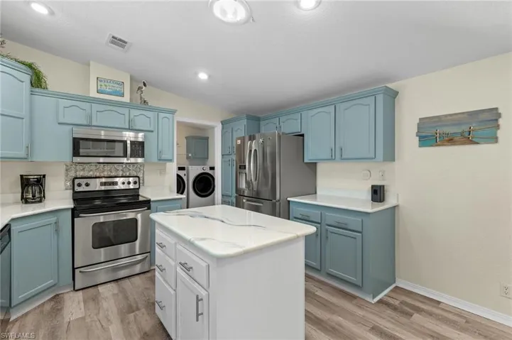 Kitchen with light hardwood / wood-style floors, stainless steel appliances, washer and dryer, a center island, and lofted ceiling
