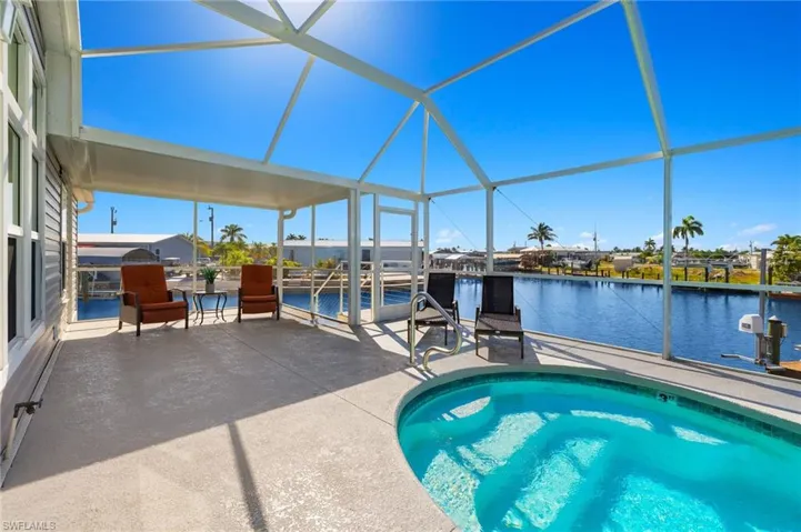 View of swimming pool featuring a patio, glass enclosure, a water view, and a jacuzzi