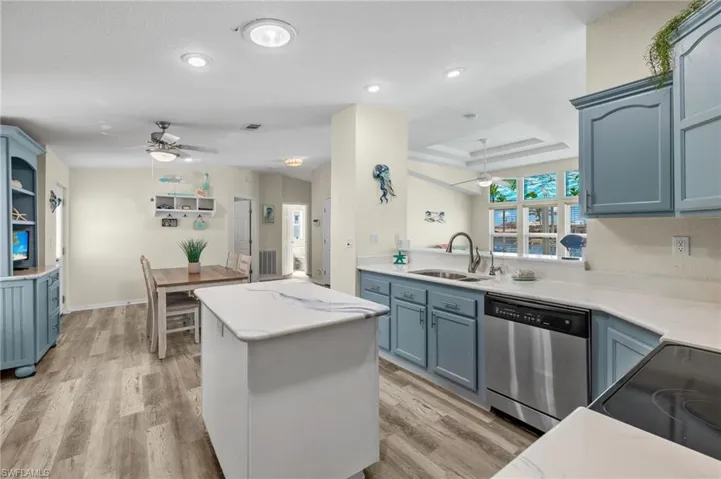 Kitchen featuring light hardwood / wood-style flooring, ceiling fan, a tray ceiling, and stainless steel dishwasher