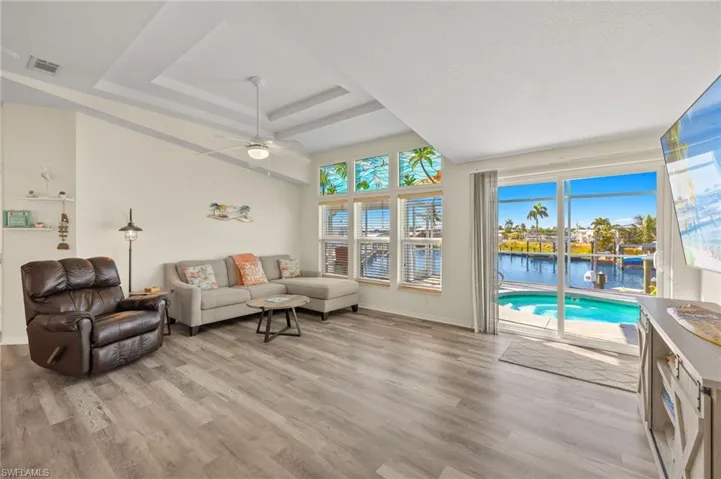 Living room featuring a tray ceiling, a water view, ceiling fan, and light wood-type flooring