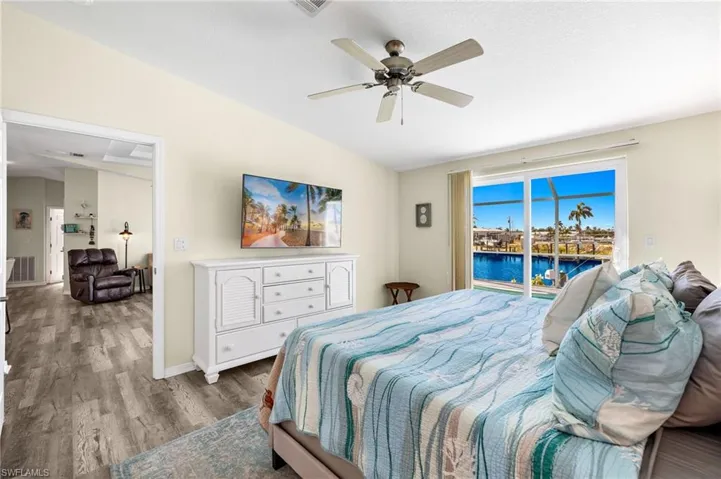 Bedroom featuring lofted ceiling, a water view, hardwood / wood-style floors, access to exterior, and ceiling fan