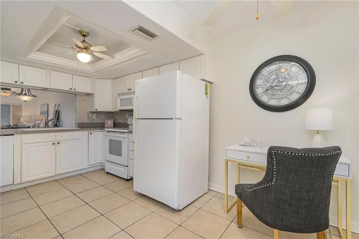 Kitchen featuring white appliances, a raised ceiling, ceiling fan, white cabinetry and extra space to curate an office or use for kitchen table.