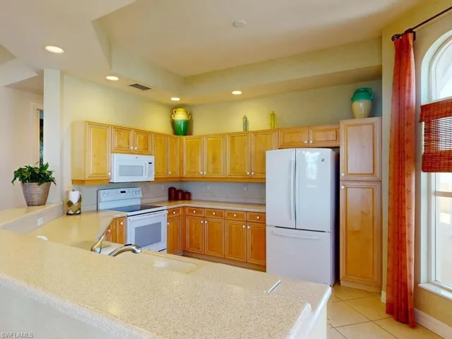 Kitchen with kitchen peninsula, sink, white appliances, and light tile patterned flooring