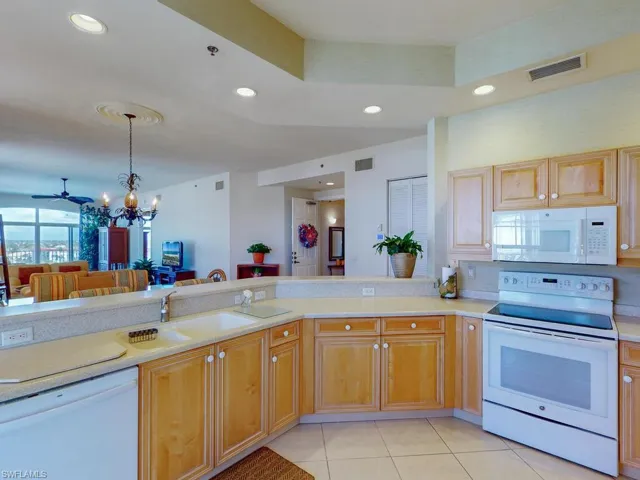 Kitchen with light tile patterned flooring, kitchen peninsula, pendant lighting, sink, and white appliances