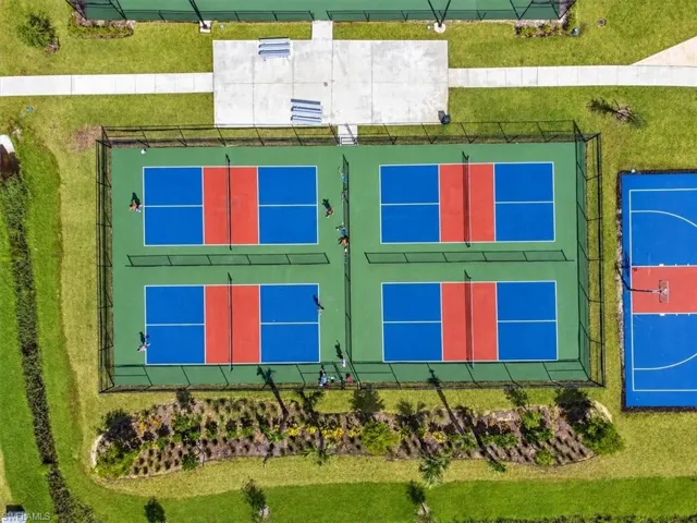 Recreational complex featuring four fenced pickleball courts and a basketball court, surrounded by manicured landscaping and paved walking paths