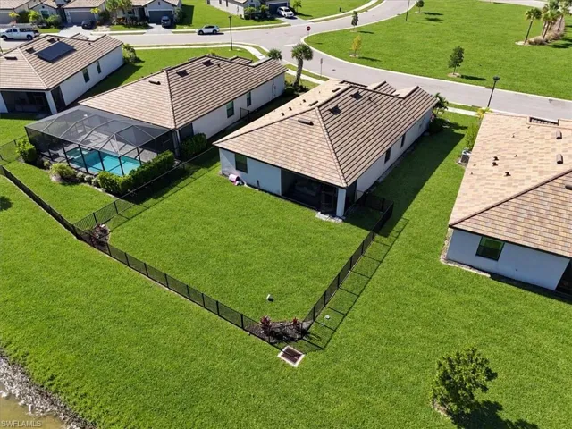 Aerial perspective of a single-story residence featuring a tiled roof, a rear-screened lanai, and a fully fenced backyard bordering a water feature