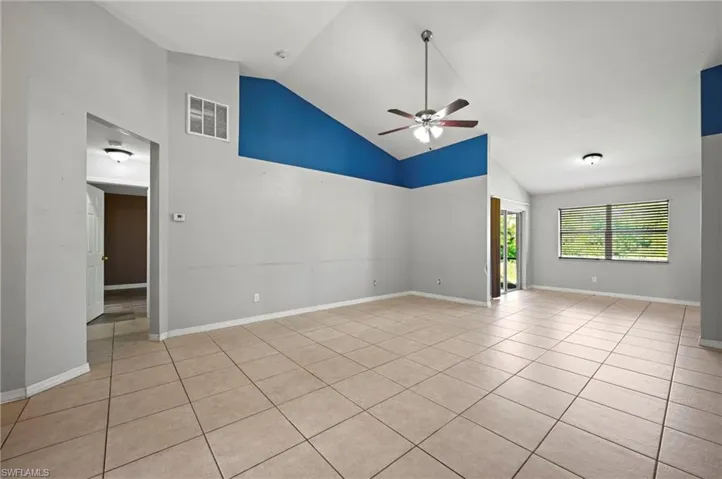 Empty room with high vaulted ceiling, light tile patterned flooring, and ceiling fan
