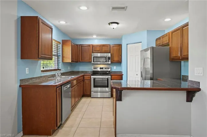 Kitchen featuring brown cabinets, stainless steel appliances, tile countertops, a peninsula, and recessed lighting