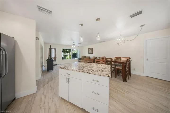 Kitchen featuring freestanding refrigerator, white cabinetry, hanging light fixtures, light wood-type flooring, and a kitchen island