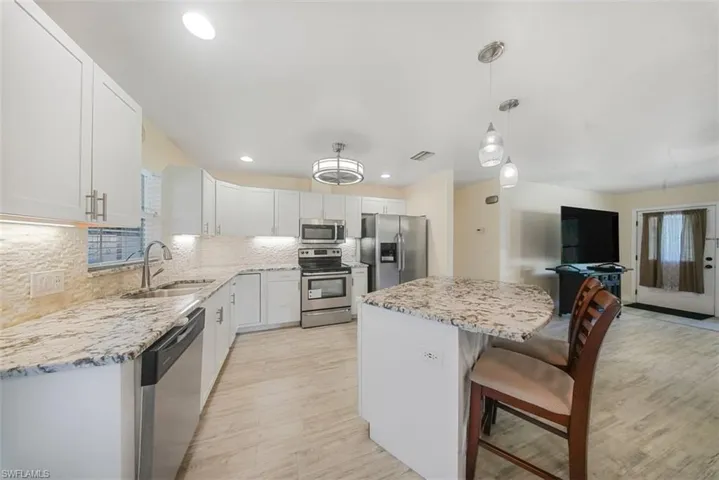 Kitchen with appliances with stainless steel finishes, a breakfast bar, a kitchen island, white cabinetry, and tasteful backsplash