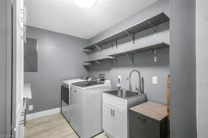 Laundry room featuring light wood-style flooring, electric panel, washing machine and clothes dryer, and cabinet space