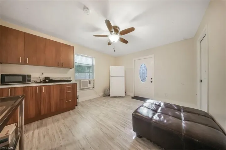Kitchen with light wood-type flooring, freestanding refrigerator, brown cabinetry, ceiling fan, and black microwave