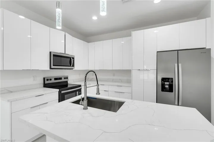 Kitchen featuring modern cabinets, stainless steel appliances, white cabinets, a center island with sink, and light stone countertops