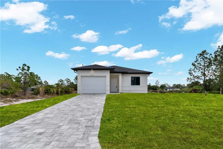 View of front of home with decorative driveway, stucco siding, a front lawn, and an attached garage