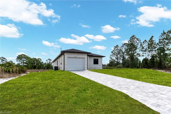 View of front facade featuring a front lawn, decorative driveway, stucco siding, and an attached garage