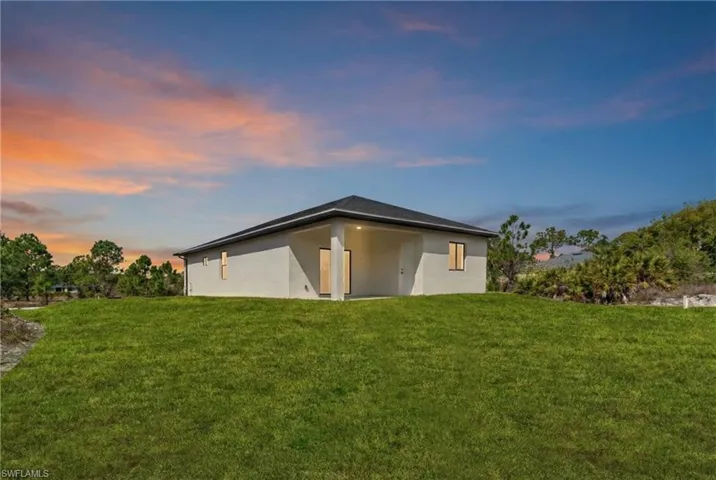 Back of house at dusk with a yard, stucco siding, and a patio