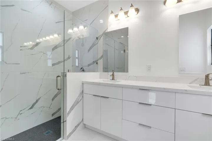 Full bathroom with double vanity, a marble finish shower, and light marble finish floors