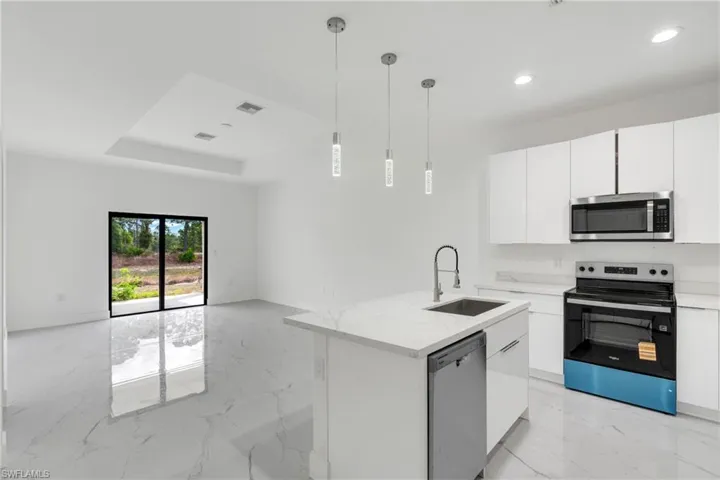 Kitchen with stainless steel appliances, white cabinets, a center island with sink, light stone countertops, and light marble finish flooring