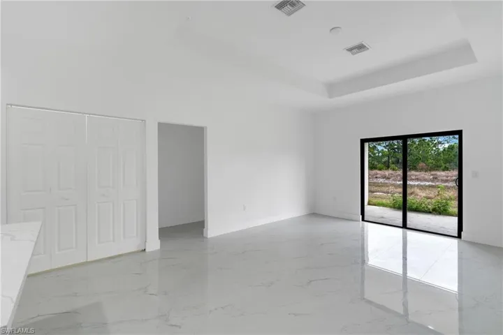 Unfurnished bedroom with a tray ceiling, access to exterior, a closet, and light marble finish floors