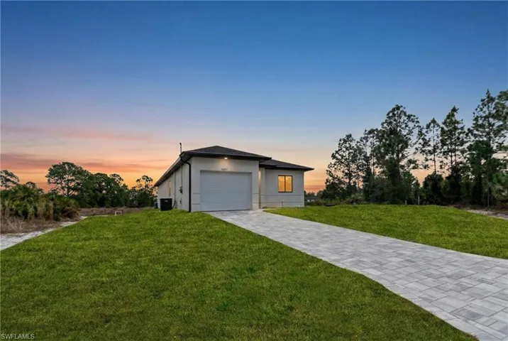 View of front of property with a yard, decorative driveway, a garage, and stucco siding
