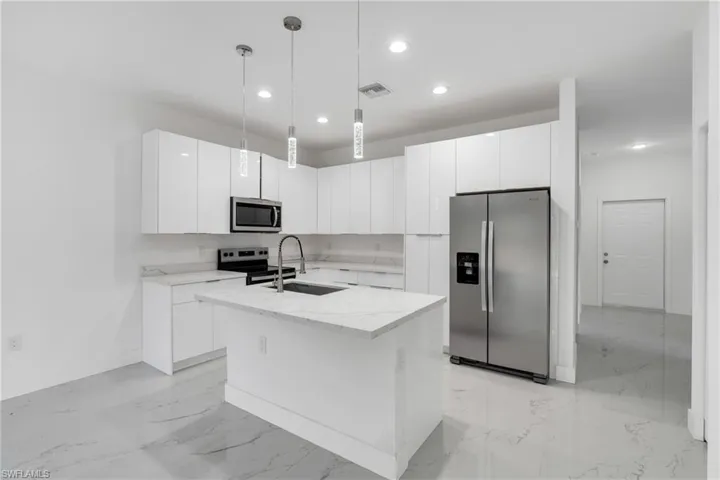 Kitchen featuring stainless steel appliances, white cabinets, hanging light fixtures, and light stone counters
