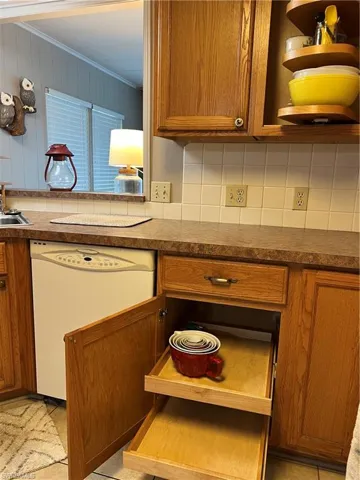 Kitchen featuring dishwashing machine, decorative backsplash, brown cabinets, and ornamental molding