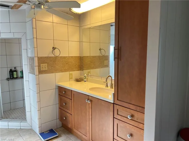 Full bathroom remodeled to make larger shower that is completely tile and with a ceiling fan, tile patterned flooring, vanity, a shower stall, and tile walls
