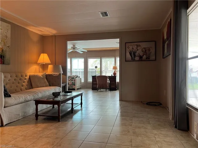 Living area featuring healthy amount of natural light, crown molding, light tile patterned flooring, a ceiling fan, and wood walls