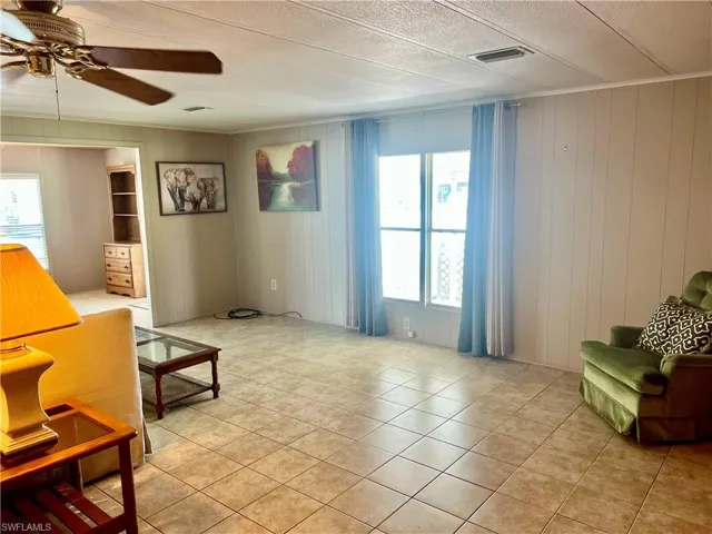Sitting room featuring light tile patterned floors, healthy amount of natural light, ceiling fan, and wood walls