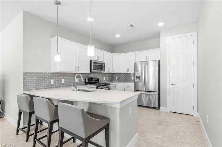 Kitchen with stainless steel appliances, decorative light fixtures, a kitchen bar, a peninsula, and white cabinetry