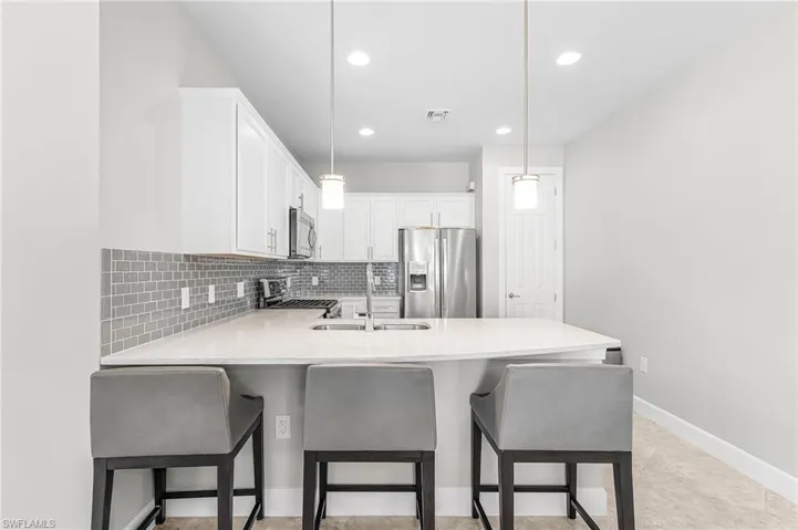Kitchen with a peninsula, white cabinets, stainless steel appliances, light stone countertops, and decorative backsplash