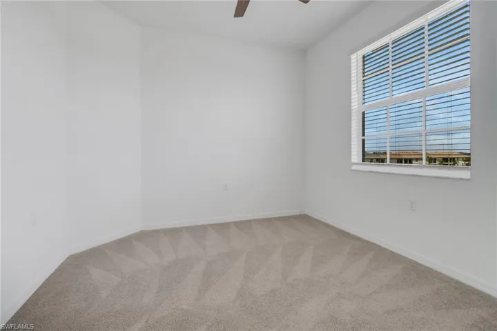 Bright room featuring a large window with horizontal blinds, neutral carpet flooring, and a ceiling fan
