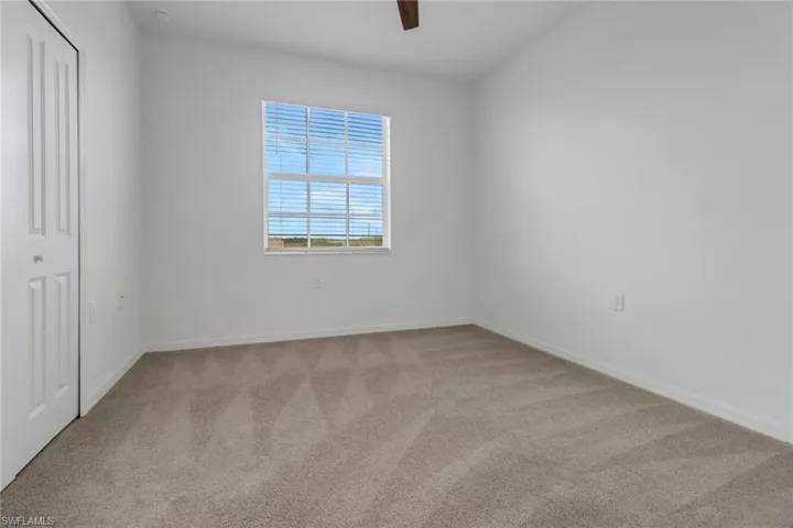 Bright room featuring a window with horizontal blinds, neutral-toned carpeting, a ceiling fan, and a white bi-fold closet door