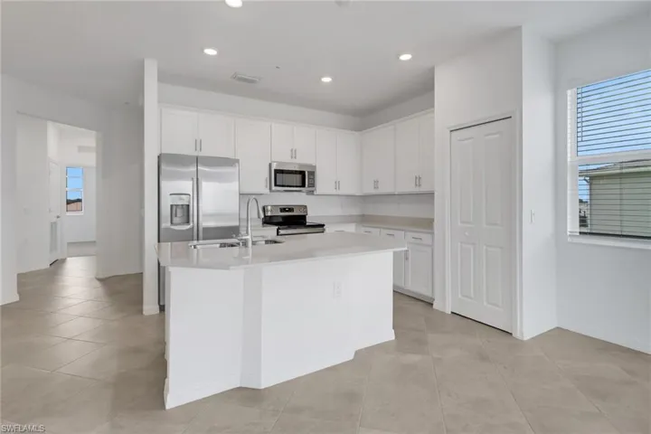 Modern kitchen featuring white cabinetry, a central island with a sink, stainless steel appliances, recessed lighting, and tile flooring
