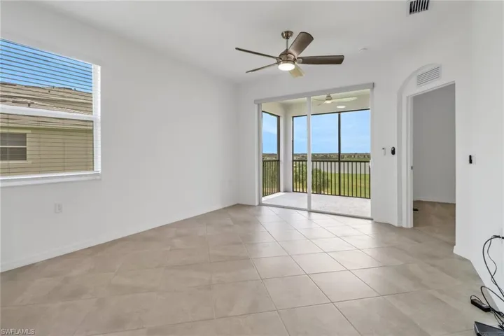 Spacious room featuring neutral tile flooring, a ceiling fan, and a large window with blinds
