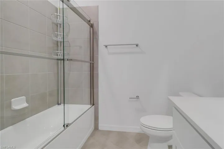 Bathroom featuring a shower/tub combination with sliding glass doors, light-toned tile surround, and an integrated soap dish