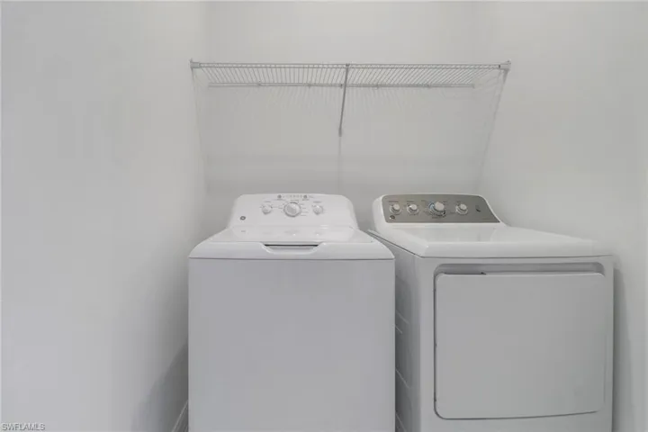 Dedicated laundry area featuring a washer and dryer set, white painted walls, and an overhead wire shelving unit