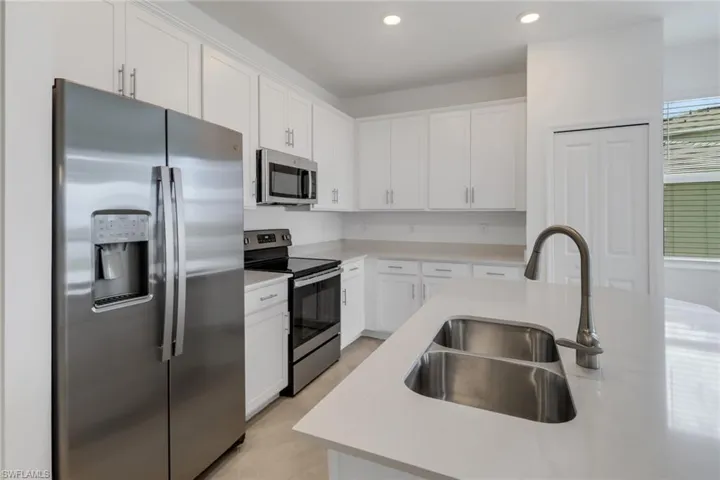 Modern kitchen featuring white cabinetry, stainless steel appliances, light countertops, a dual basin stainless steel sink, and recessed lighting