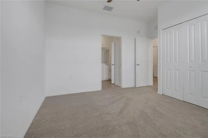 Carpeted room with white walls, featuring a white bi-fold closet and an open doorway leading to a bathroom with a white vanity and mirror