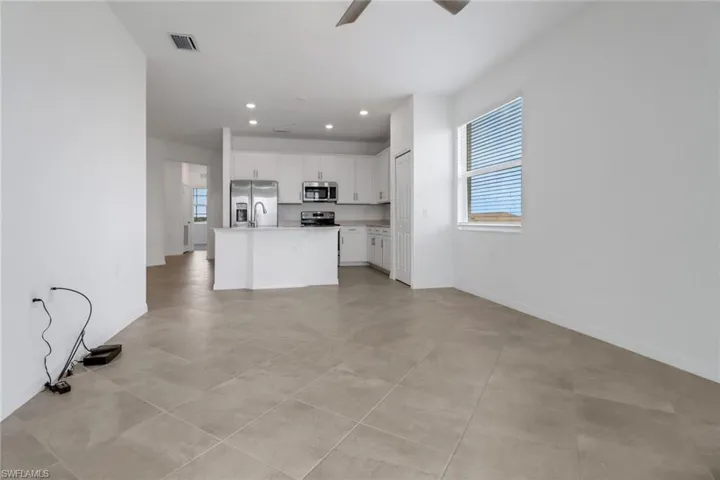 Open-concept living area featuring large format tile flooring, a kitchen island with sink, stainless steel appliances, white cabinetry, and recessed lighting
