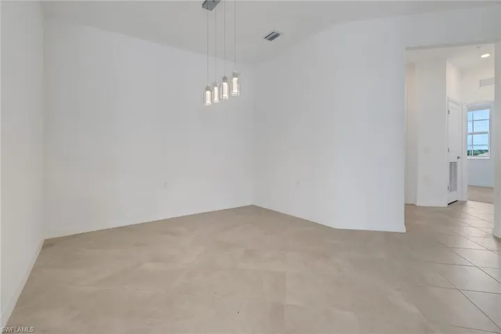 Spacious room featuring light-toned tile flooring, neutral wall tones, and a contemporary multi-light pendant fixture