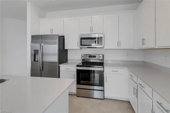 Modern kitchen featuring white shaker cabinetry, stainless steel appliances, light-toned countertops, and an integrated kitchen island