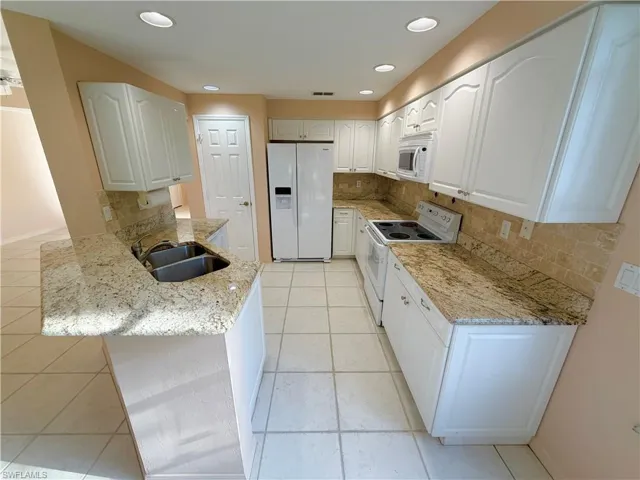 Kitchen with white appliances, backsplash, white cabinets, light tile patterned floors, and recessed lighting