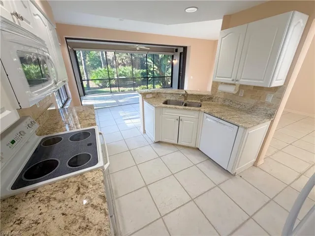 Kitchen featuring light stone counters, white cabinetry, white appliances, a peninsula, and light tile patterned flooring