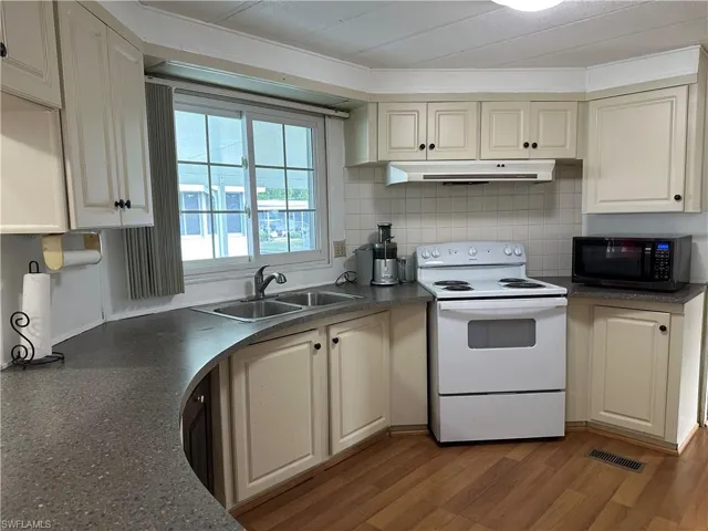 Kitchen featuring white range with electric stovetop, dark countertops, black microwave, wood finished floors, and under cabinet range hood