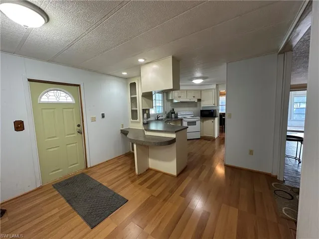 Kitchen with a kitchen breakfast bar, dark countertops, a peninsula, light wood finished floors, and electric range