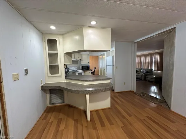 Kitchen featuring a kitchen breakfast bar, light wood finished floors, white appliances, white cabinetry, and a peninsula