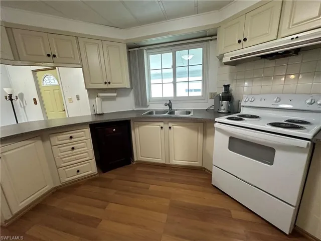 Kitchen featuring white electric range oven, under cabinet range hood, dark wood finished floors, and dark countertops