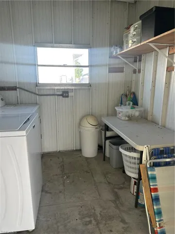 Laundry area with wood walls, unfinished concrete flooring, and washer and clothes dryer